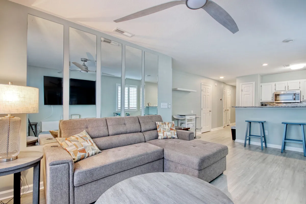 A bright, open-plan living area featuring a comfortable sofa, coffee table, TV, and a stylish bar area. Sunlight streams in through large windows, creating an inviting setting for relaxation, socializing, and shared moments.