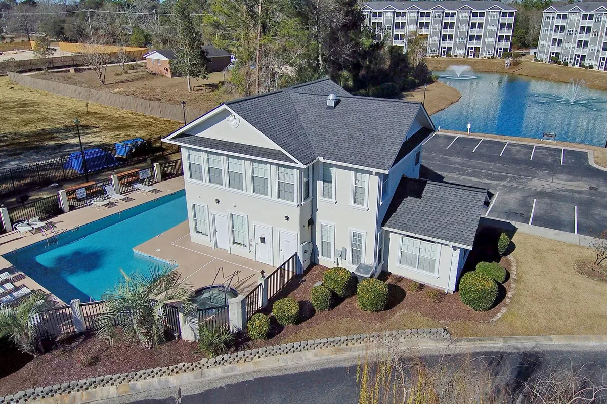 A sparkling swimming pool set within a landscaped garden, adjacent to a modern building. Poolside seating offers space for families to relax and play. The scene is bright and inviting, evoking the fun and leisure of a resort-style community.