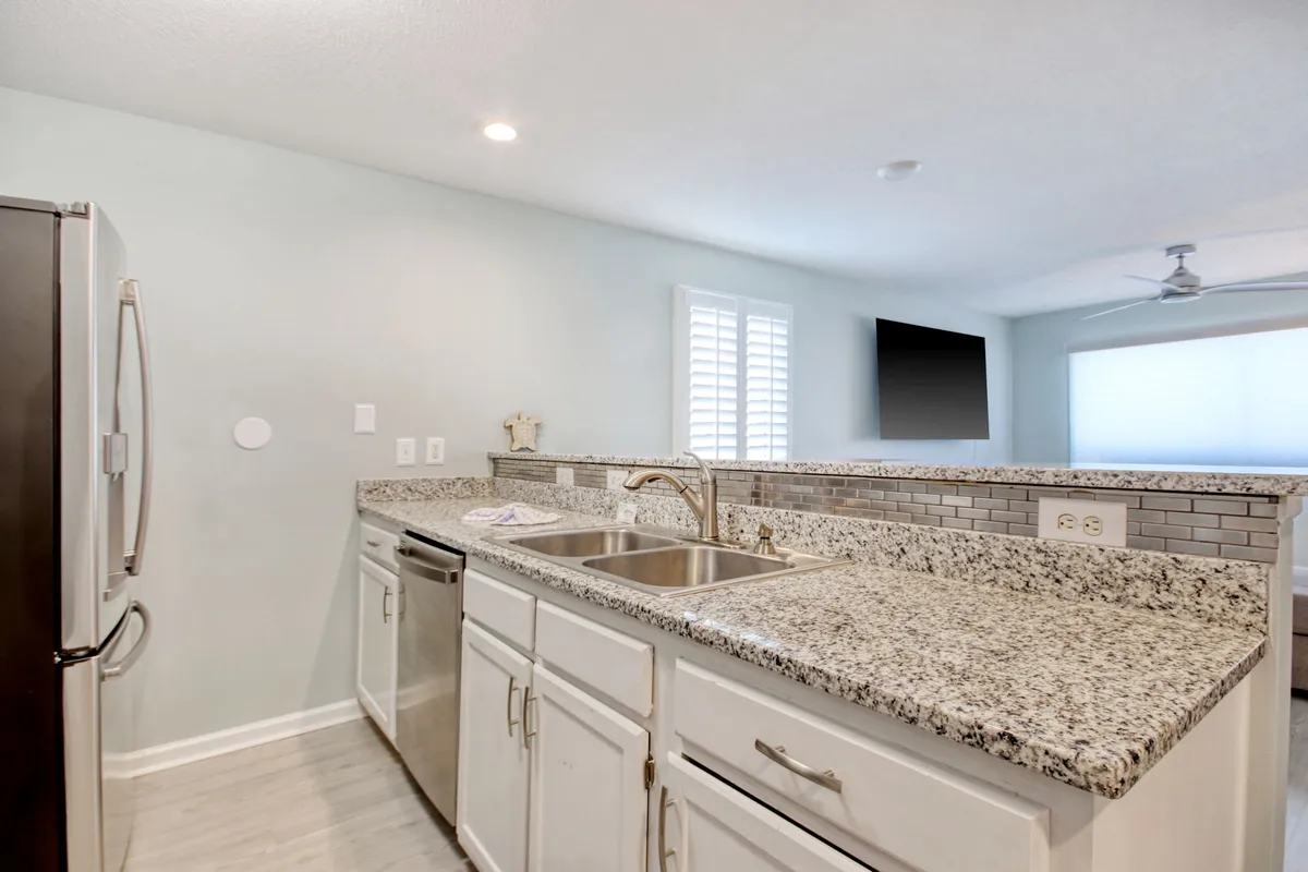 This image showcases a modern kitchen with granite countertops and stainless steel appliances. A window with blinds lets in natural light, and the open layout makes it ideal for cooking and connecting with family or guests. The scene is lively and inviting, reflecting moments of cooking, entertaining, and gathering.