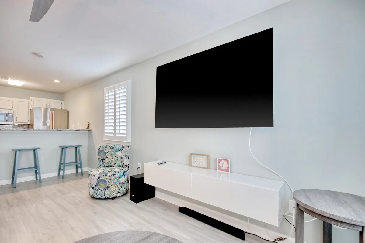 A cozy living space with a large wall-mounted TV, a colorful accent chair, and a modern white media console. The area is designed for both entertainment and casual conversation, with bright, comfortable furnishings.