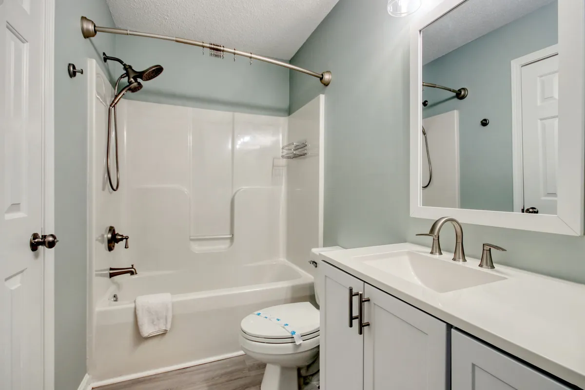 A bright, modern bathroom showcasing a glass-enclosed shower, a wide vanity with mirror, and fresh towel accents, suggesting an inviting and refreshing space for daily routines.