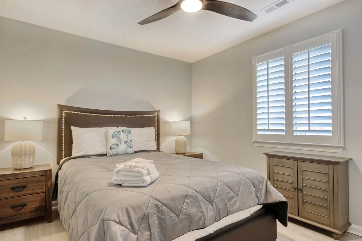 A serene bedroom scene featuring a neatly made bed flanked by nightstands and lamps, with soft window treatments allowing gentle natural light to filter in, creating a restful and inviting atmosphere.