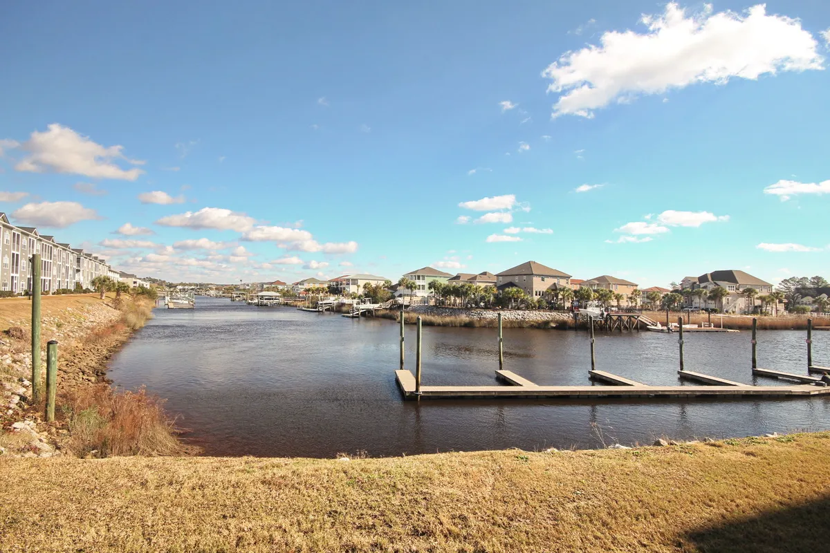 This image showcases a tranquil waterfront scene with calm water, a dock extending out, residential buildings in the background, and an expansive sky overhead. The setting invites boating, fishing, and relaxing by the water, embodying the essence of an active waterfront lifestyle.