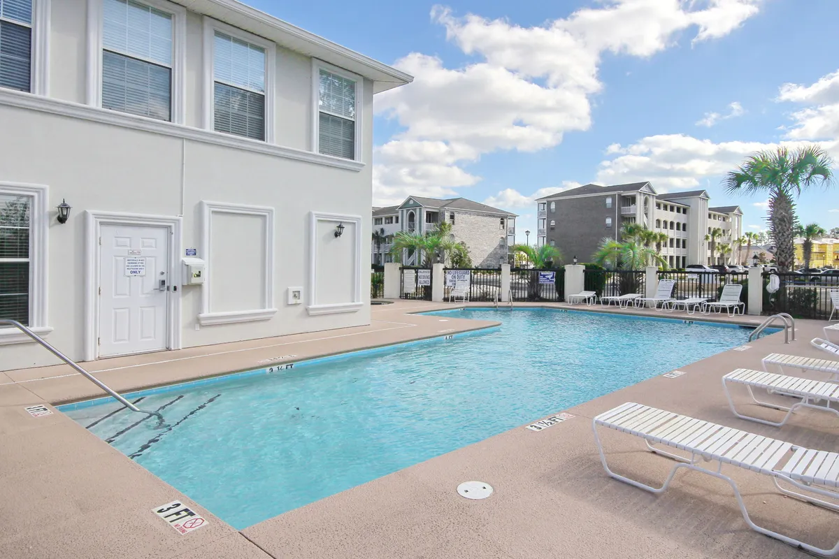 A vibrant exterior scene featuring a sparkling swimming pool surrounded by palm trees and comfortable lounge chairs. The pool area is designed for both relaxation and socializing, with ample space for residents to gather for sunset swims or poolside barbecues.