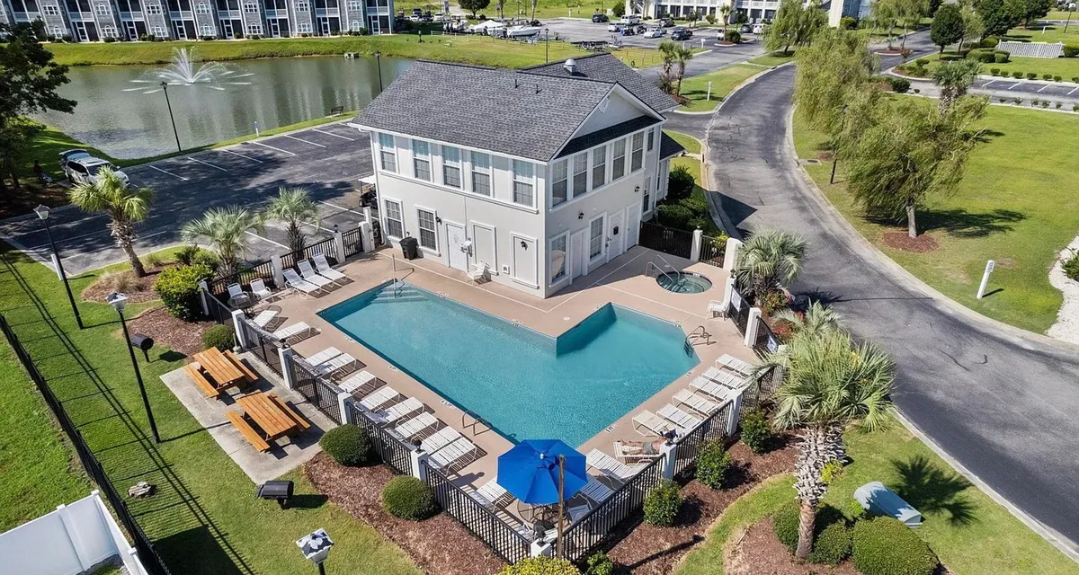 An inviting swimming pool area with outdoor seating, lush landscape greenery, and a decorative water fountain. The setting is ideal for swimming, sunbathing, or enjoying community events and gatherings.