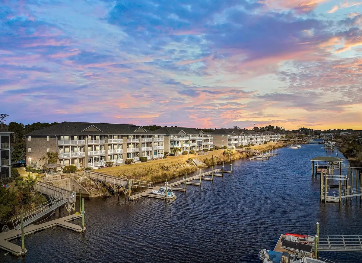 A serene waterway with docks and residential buildings visible in the background. The sky is calm, and the overall mood is peaceful, suggesting opportunities for boating, fishing, or just enjoying the view from the resort-like setting.